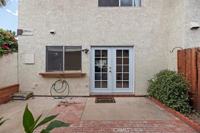 entrance to property with french doors, a patio area, stucco siding, and fence