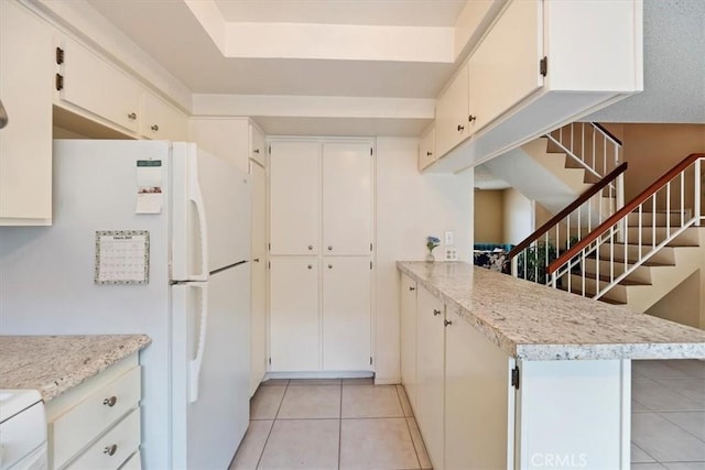 kitchen with white cabinets, a peninsula, freestanding refrigerator, and light tile patterned floors