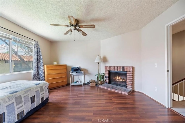 bedroom featuring a brick fireplace, a ceiling fan, wood finished floors, and a textured ceiling