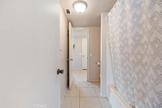 hallway featuring visible vents, baseboards, and light tile patterned flooring