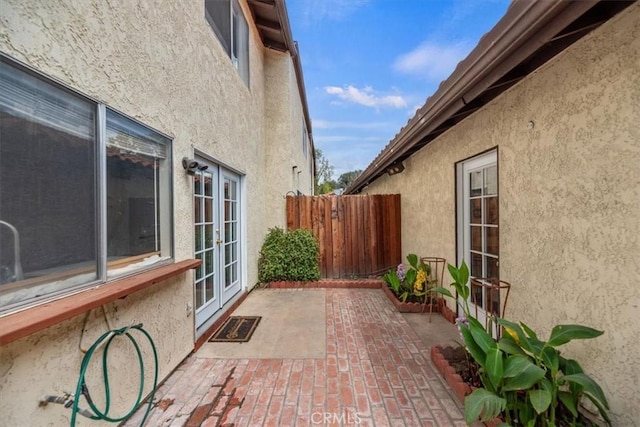 view of side of property with french doors, fence, and stucco siding