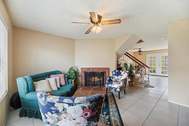 tiled living area featuring baseboards, a brick fireplace, a ceiling fan, a textured ceiling, and stairs