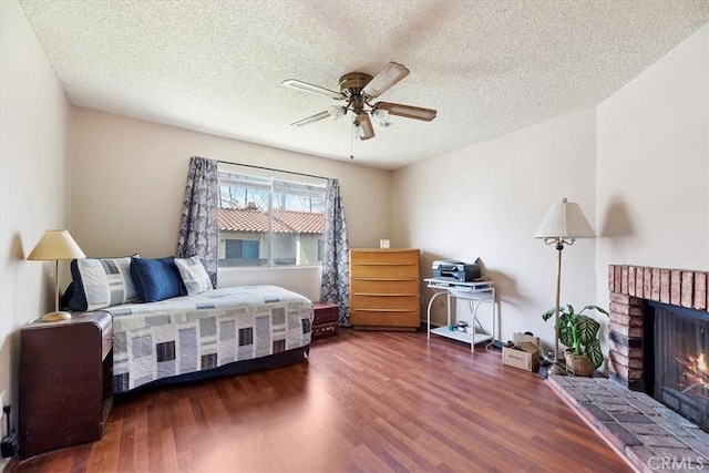 bedroom with a brick fireplace, ceiling fan, wood finished floors, and a textured ceiling