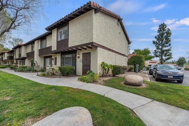 view of property exterior with a yard, stucco siding, and a tiled roof