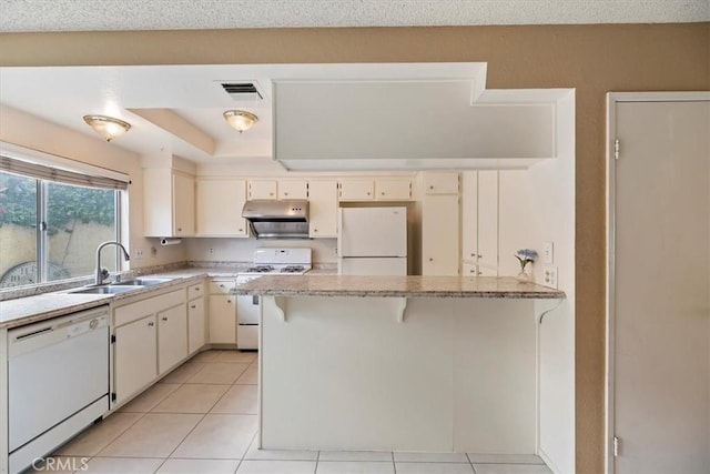 kitchen featuring white appliances, a peninsula, visible vents, under cabinet range hood, and a sink
