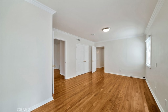 empty room featuring light wood-style flooring, crown molding, baseboards, and visible vents