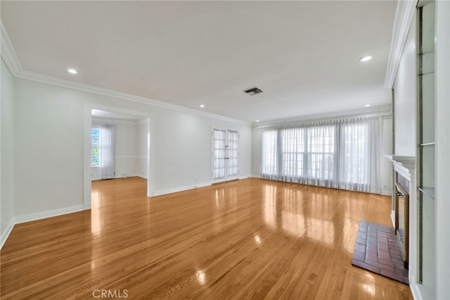 unfurnished living room featuring light wood-style flooring, ornamental molding, a glass covered fireplace, and visible vents