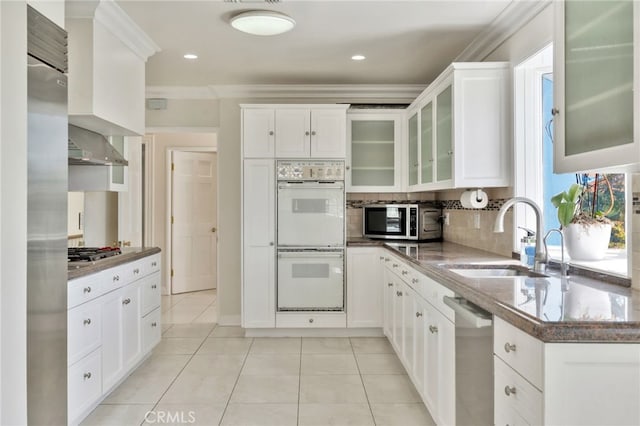 kitchen with wall chimney exhaust hood, appliances with stainless steel finishes, light tile patterned flooring, a sink, and decorative backsplash