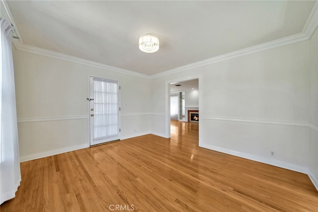 empty room with a lit fireplace, light wood-type flooring, crown molding, and baseboards