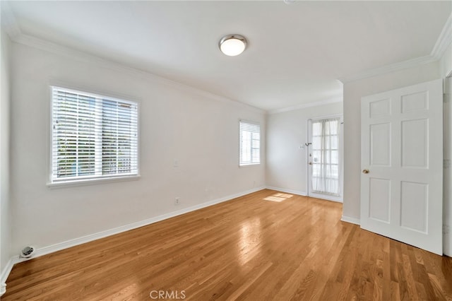 spare room with crown molding, baseboards, and light wood-type flooring