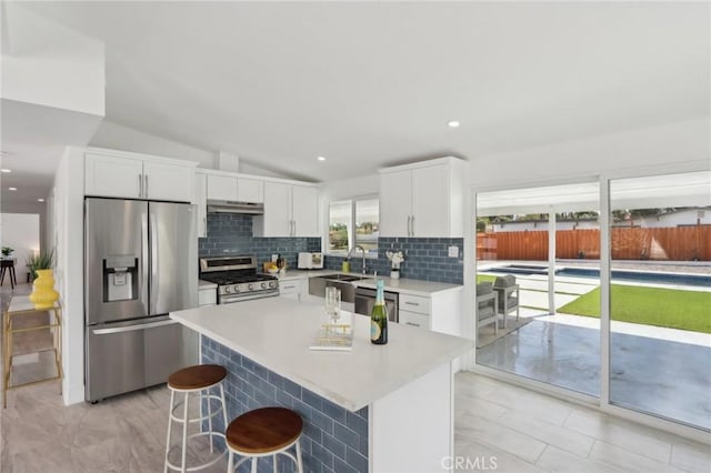 845 W Gateway Dr, Palm Springs, CA 92262 - kitchen featuring appliances with stainless steel finishes, under cabinet range hood, tasteful backsplash, a breakfast bar area, and white cabinets