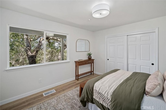 bedroom featuring wood finished floors, baseboards, a closet, and visible vents