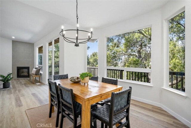 dining space featuring a wealth of natural light, light wood-style flooring, a large fireplace, and an inviting chandelier
