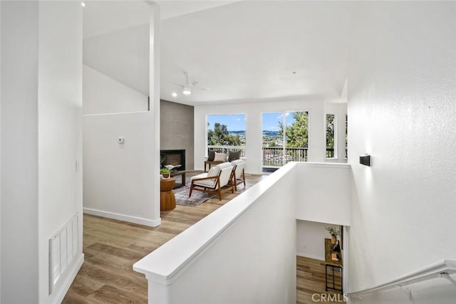 stairs featuring visible vents, baseboards, a ceiling fan, wood finished floors, and a large fireplace