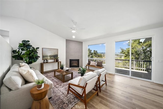 living room with baseboards, light wood-type flooring, a ceiling fan, lofted ceiling, and a tile fireplace