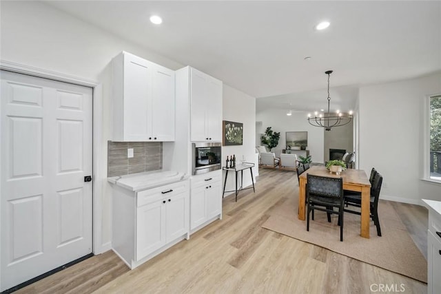 kitchen with tasteful backsplash, an inviting chandelier, light wood-style floors, stainless steel microwave, and white cabinetry