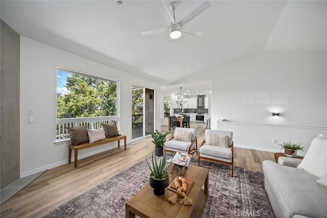 living area with baseboards, vaulted ceiling, light wood-style floors, and ceiling fan with notable chandelier