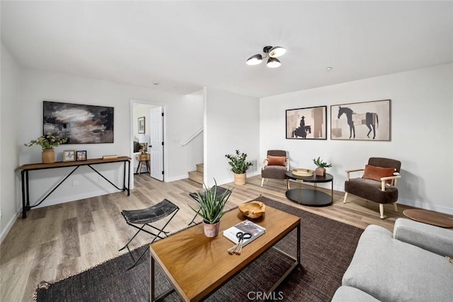 living area with light wood-style flooring, stairway, and baseboards
