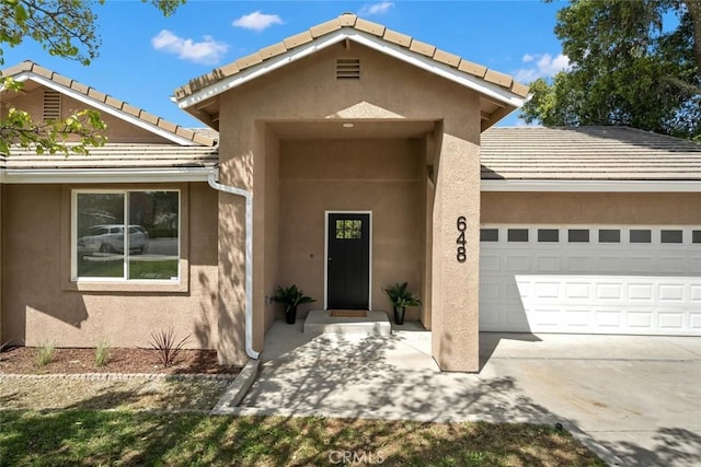 doorway to property with an attached garage, driveway, stucco siding, and a tile roof