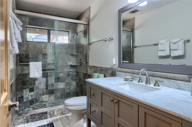 bathroom with tile walls, visible vents, toilet, vanity, and a stall shower