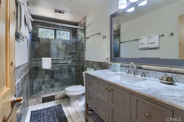 full bath featuring a stall shower, toilet, vanity, visible vents, and tile walls