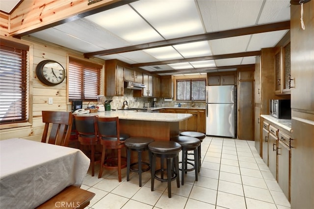 kitchen with a kitchen breakfast bar, light tile patterned floors, under cabinet range hood, a peninsula, and appliances with stainless steel finishes