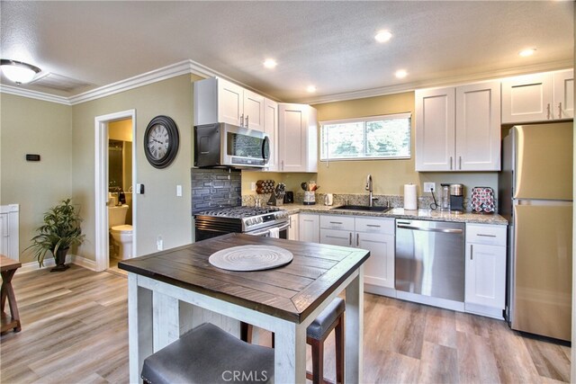41548 Hutchison Ct, Murrieta, CA 92562 - kitchen featuring appliances with stainless steel finishes, a sink, light wood-style floors, crown molding, and white cabinetry