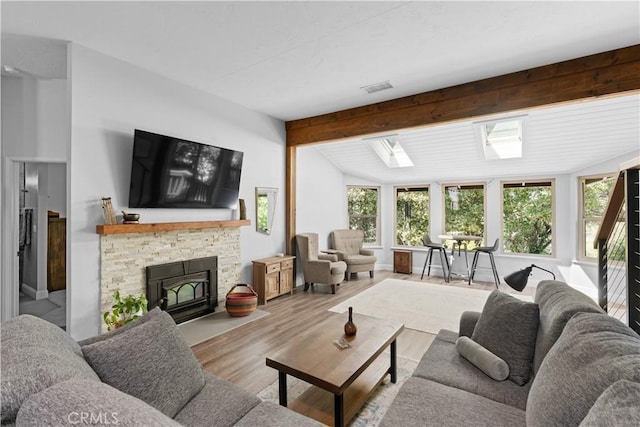 living room featuring vaulted ceiling with skylight, a stone fireplace, wood finished floors, and visible vents