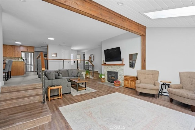 living area with beam ceiling, recessed lighting, a fireplace with flush hearth, light wood-type flooring, and a skylight