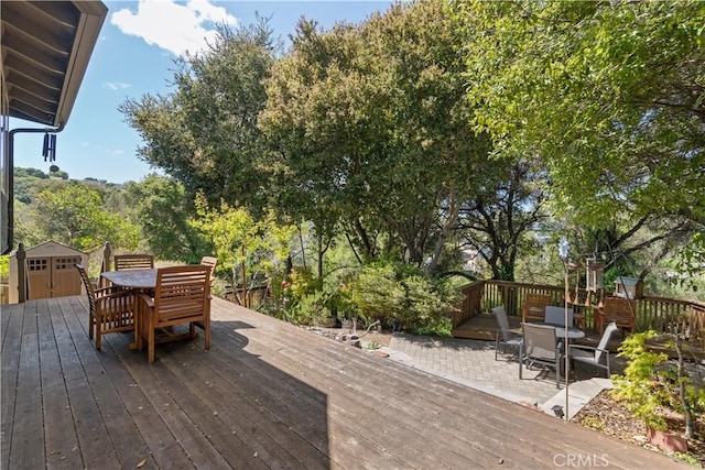 wooden terrace featuring outdoor dining area, an outbuilding, and a storage shed