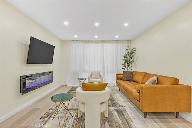 living room with baseboards, a glass covered fireplace, light wood-style floors, and recessed lighting