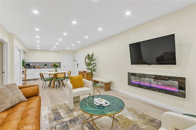 living area with light wood-style flooring, a glass covered fireplace, and recessed lighting