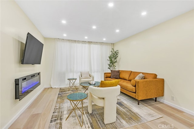 living room featuring baseboards, recessed lighting, a glass covered fireplace, and light wood-style floors