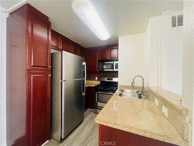 kitchen with light wood-type flooring, visible vents, a sink, reddish brown cabinets, and stainless steel appliances