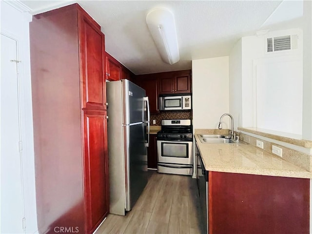 kitchen featuring visible vents, a sink, appliances with stainless steel finishes, dark brown cabinets, and light wood-style flooring