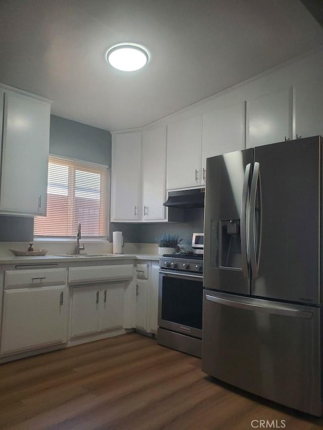 kitchen featuring a sink, under cabinet range hood, white cabinetry, light countertops, and appliances with stainless steel finishes