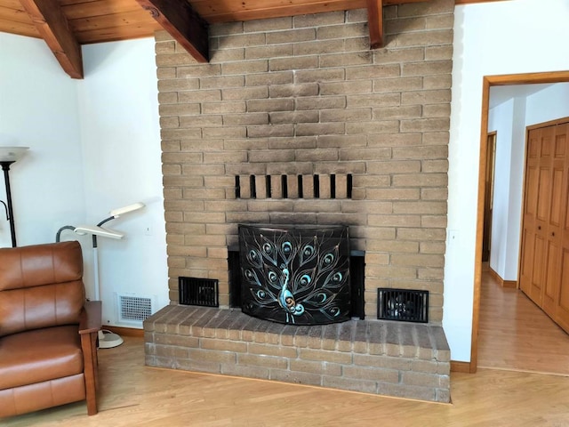living area with wood finished floors, visible vents, beamed ceiling, and a brick fireplace