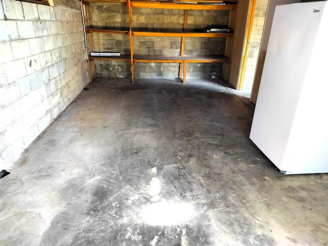 below grade area with freestanding refrigerator and concrete block wall