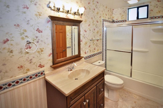 bathroom with combined bath / shower with glass door, vanity, wallpapered walls, toilet, and wainscoting