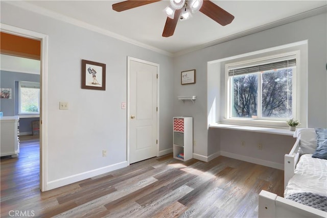 living area with baseboards, wood finished floors, ornamental molding, and a ceiling fan