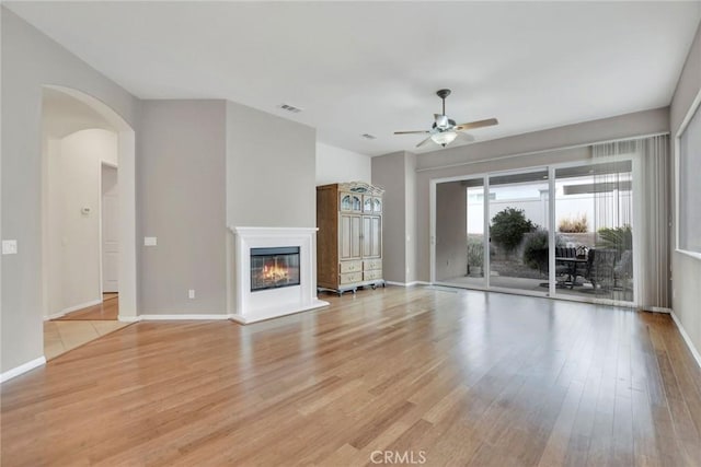 unfurnished living room with light wood-style flooring, a glass covered fireplace, and a ceiling fan