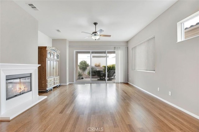 unfurnished living room featuring baseboards, visible vents, a ceiling fan, a glass covered fireplace, and wood finished floors