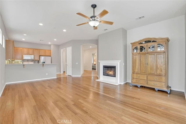 unfurnished living room with arched walkways, ceiling fan, visible vents, and light wood finished floors