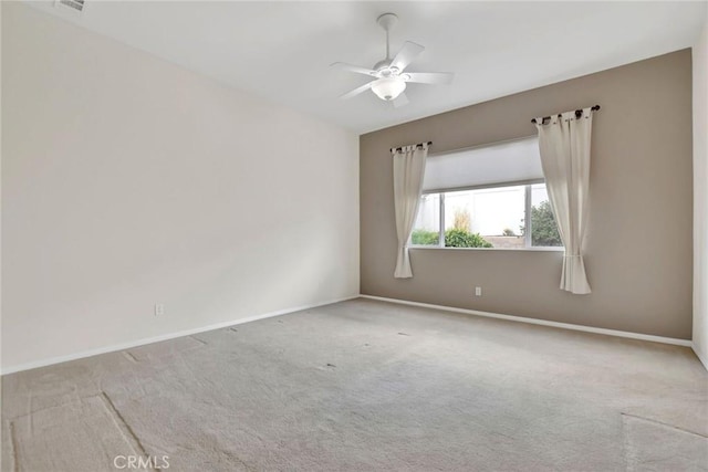 carpeted spare room featuring baseboards and a ceiling fan