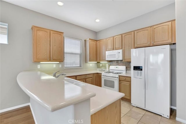 kitchen with a peninsula, light countertops, light brown cabinetry, and white appliances