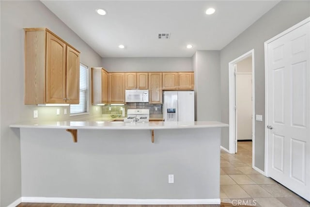 kitchen featuring light countertops, visible vents, a peninsula, white appliances, and a breakfast bar area