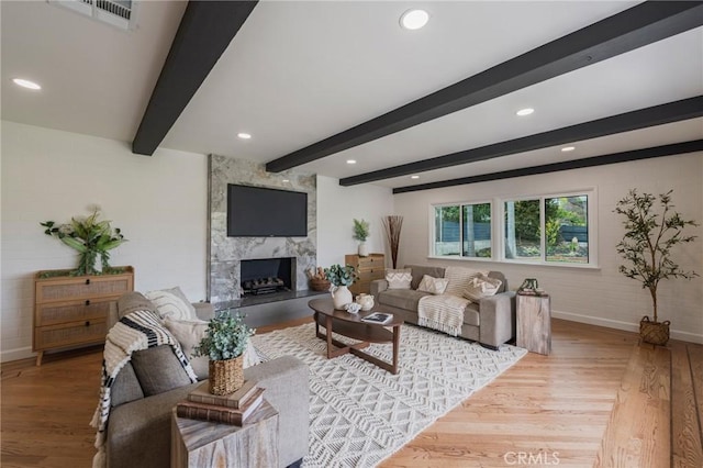 living room with visible vents, a fireplace, wood finished floors, baseboards, and beamed ceiling