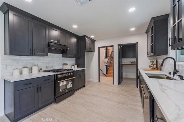 kitchen featuring light stone counters, a sink, visible vents, under cabinet range hood, and gas range oven