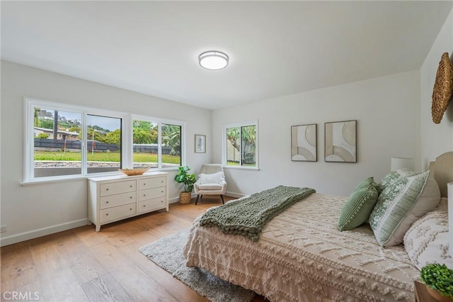 bedroom featuring baseboards, multiple windows, and light wood finished floors