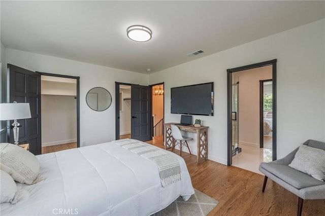 bedroom featuring a spacious closet, baseboards, wood finished floors, and visible vents